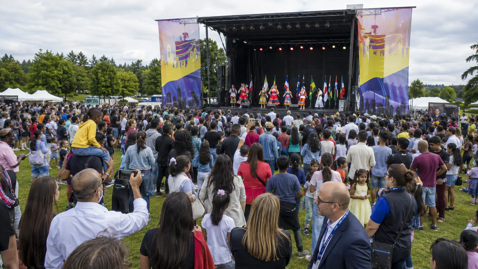 Dancers in traditional dress performing on a large outdoor stage in front of a packed festival crowd